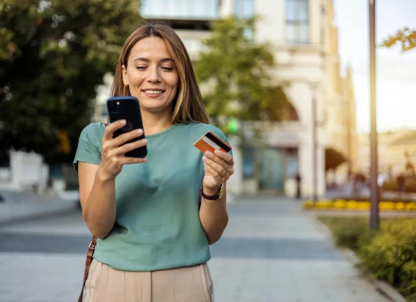 Woman holding a Credit One credit card while reviewing robocall settlement information on her phone