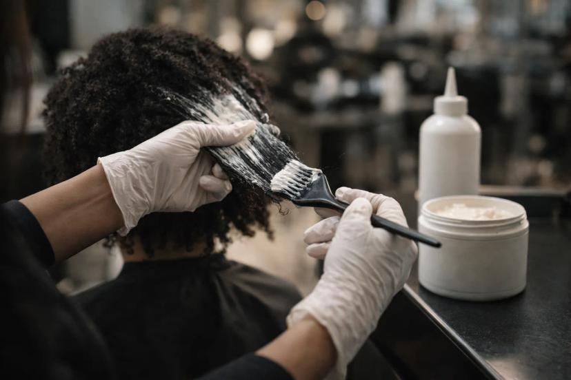 Hair stylist applying unbranded chemical hair relaxer during salon treatment